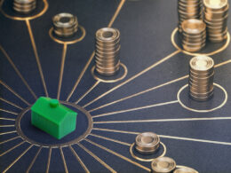 A monopoly style toy house at the centre of stacks of gold coins. Representing property finance diversity.