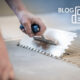 Close-up of a hand spreading tile adhesive with a notched trowel, with title 'blog'