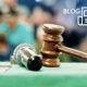 Close-up of a wooden gavel and a microphone on a green table, with a blurred crowd in the background for an auction room post.